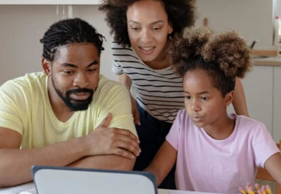 A family looks at a computer screen together over their kitchen table.