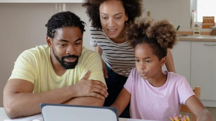 A family looks at a computer screen together over their kitchen table.