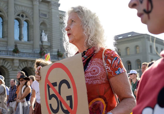 Woman holds sign protesting 5G outisde courthouse as part of a larger gathering.