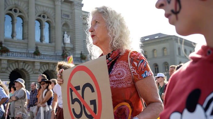 Woman holds sign protesting 5G outisde courthouse as part of a larger gathering.