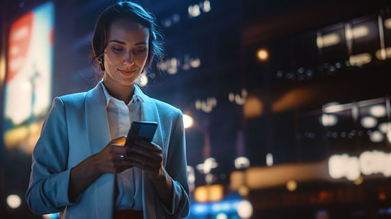 Woman using smartphone walking through night city street full of neon lights
